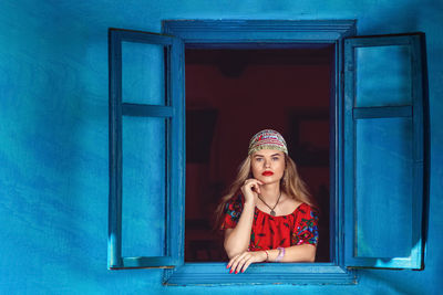 Portrait of beautiful gypsy fortune and horoscope witch teller woman in red dress standing at window