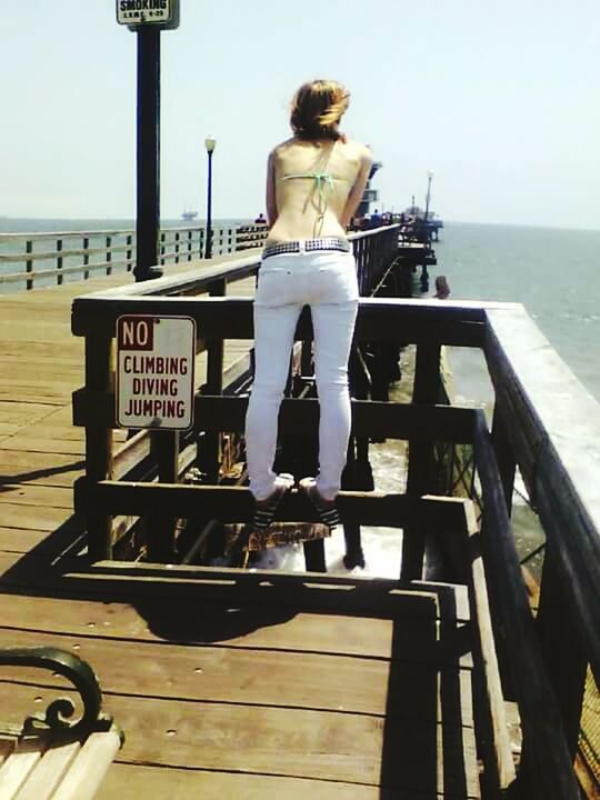 sea, water, horizon over water, clear sky, pier, railing, sky, beach, relaxation, rear view, wood - material, sunlight, tranquil scene, person, tranquility, nature, lifestyles, shore, day