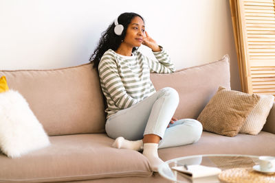 Young woman using phone while sitting on sofa at home