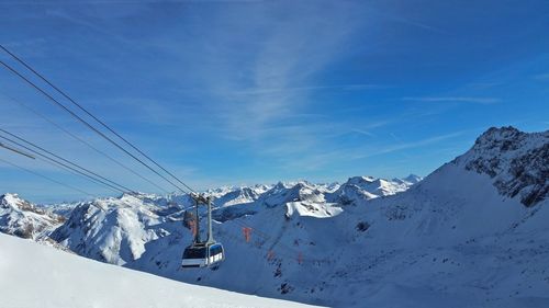 Ski lift over snowcapped mountains against blue sky
