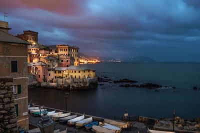 Scenic view of sea and houses against cloudy sky at dusk