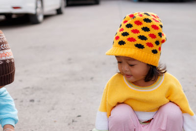 Cute girl looking away while crouching on street