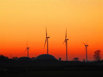 Silhouette wind turbines on field against orange sky