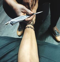 Low section of person making henna tattoo on woman leg