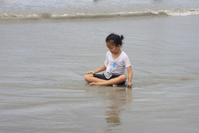 Rear view of a girl sitting on sand of beach.