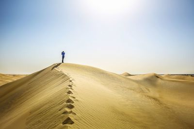 Boy photographing while standing on sand dune in desert against sky
