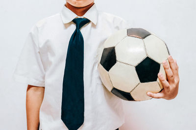 Midsection of male student holding soccer ball against white background