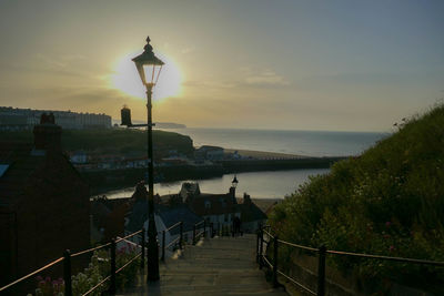 Street amidst sea and buildings against sky during sunset