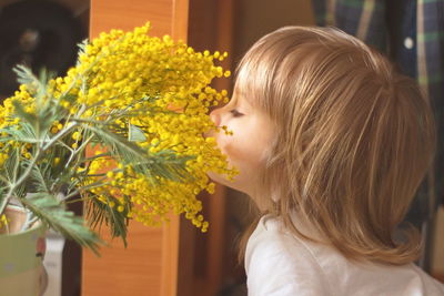 Close-up side view of cute baby girl smelling yellow flowering plants at home