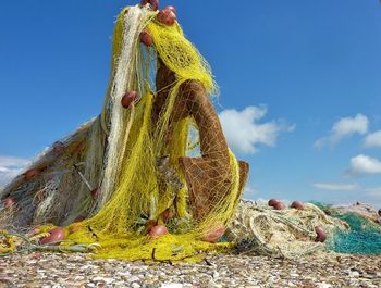 Low angle view of anchor covered with fishing net against blue sky on sunny day