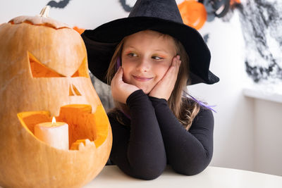 Cute girl in costume of witch with pumpkin at home, having fun, celebrating halloween