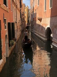 Reflection of man on gondola in canal amidst buildings