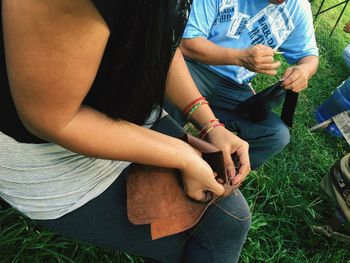 Midsection of man stitching leather while sitting at field