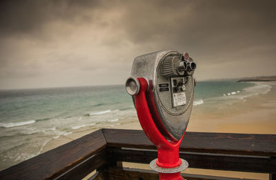 Close-up of coin-operated binoculars by sea against sky