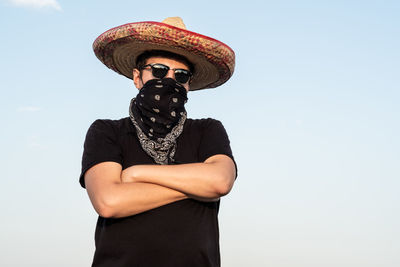 Young man wearing hat with arms crossed standing against clear sky