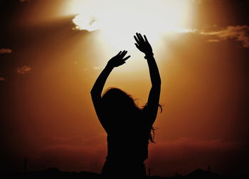 Silhouette woman standing with arms raised against orange sky during sunset