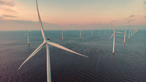 Low angle view of wind turbines on field against sky during sunset