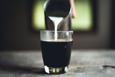 Cropped hand pouring milk in coffee on table