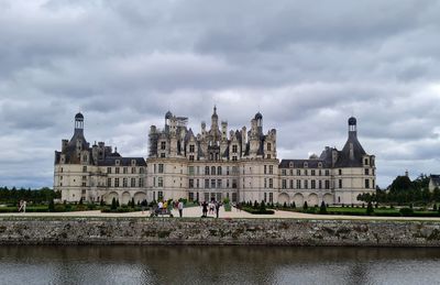 Buildings by river against cloudy sky