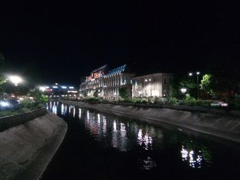 Illuminated buildings by river against sky in city at night