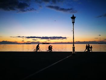Silhouette people walking on beach against sky during sunset