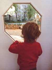 Rear view of boy looking through window in park