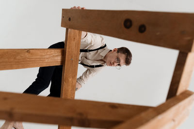 Low angle view of young man with wooden ladder against white background