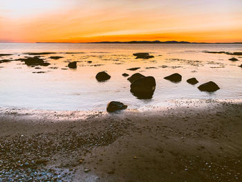 Rocks on beach against sky during sunset