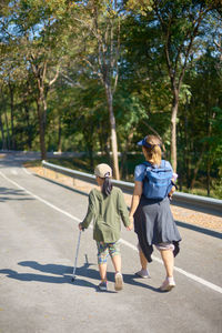 Rear view of mother and daughter walking on road against trees