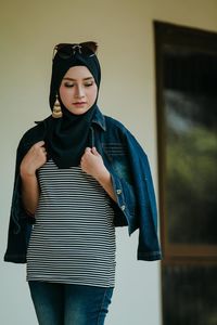 Portrait of young woman standing against wall