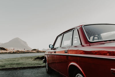 Side view of antique red automobile on road passing through mountain on cloudy day