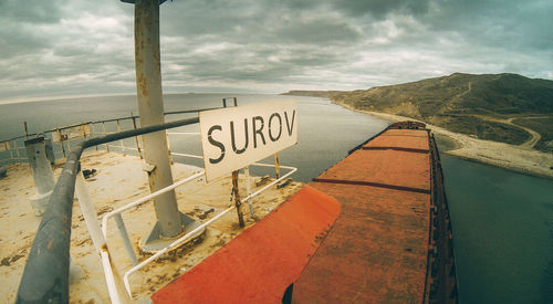 Text on railing by sea against sky