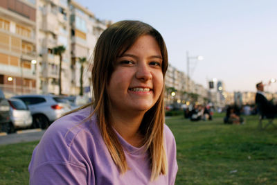 Portrait of smiling woman sitting in city during sunset