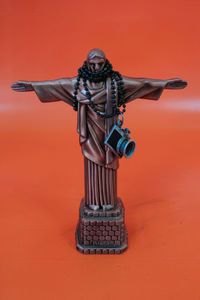 Jesus christ statue with beaded necklace and camera on orange background