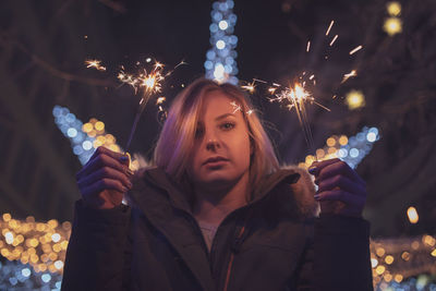 Portrait of woman holding illuminated sparkler at night