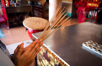 Cropped hands holding incense sticks while praying in temple