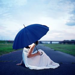 Side view of woman with umbrella sitting on road