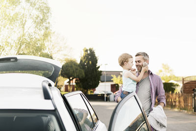 Father carrying son with stuffed toy while standing by car on street