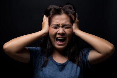 Scared young woman screaming while standing against black background