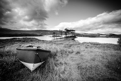 Abandoned boat on field by sea against sky