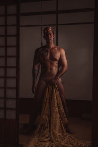 Shirtless man standing against wall