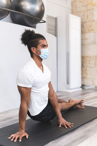 Young man stretching on exercise mat at yoga studio during pandemic