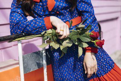 Midsection of woman leaning on railing with rose in hand