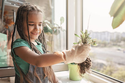 Happy girl holding flower pot against window