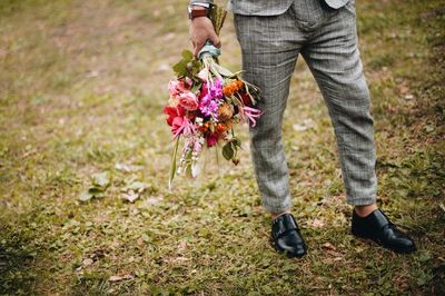 Low section of man holding bouquet while standing on grassy field