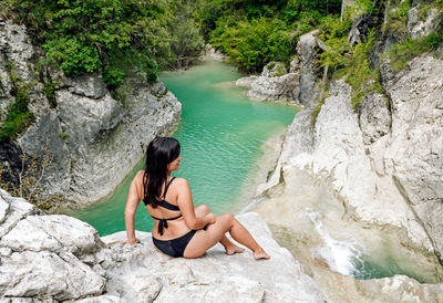 Young woman in bikini sitting on rock by river, waterfall. bikini, outdoors, beautiful girl.