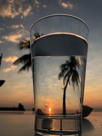 Close-up of beer glass on table against sunset sky