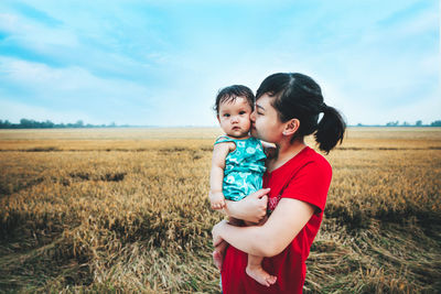 Siblings standing on field against sky