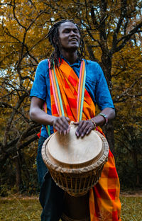 Man playing musical instrument while standing against trees