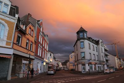 Vehicles on road against buildings at sunset